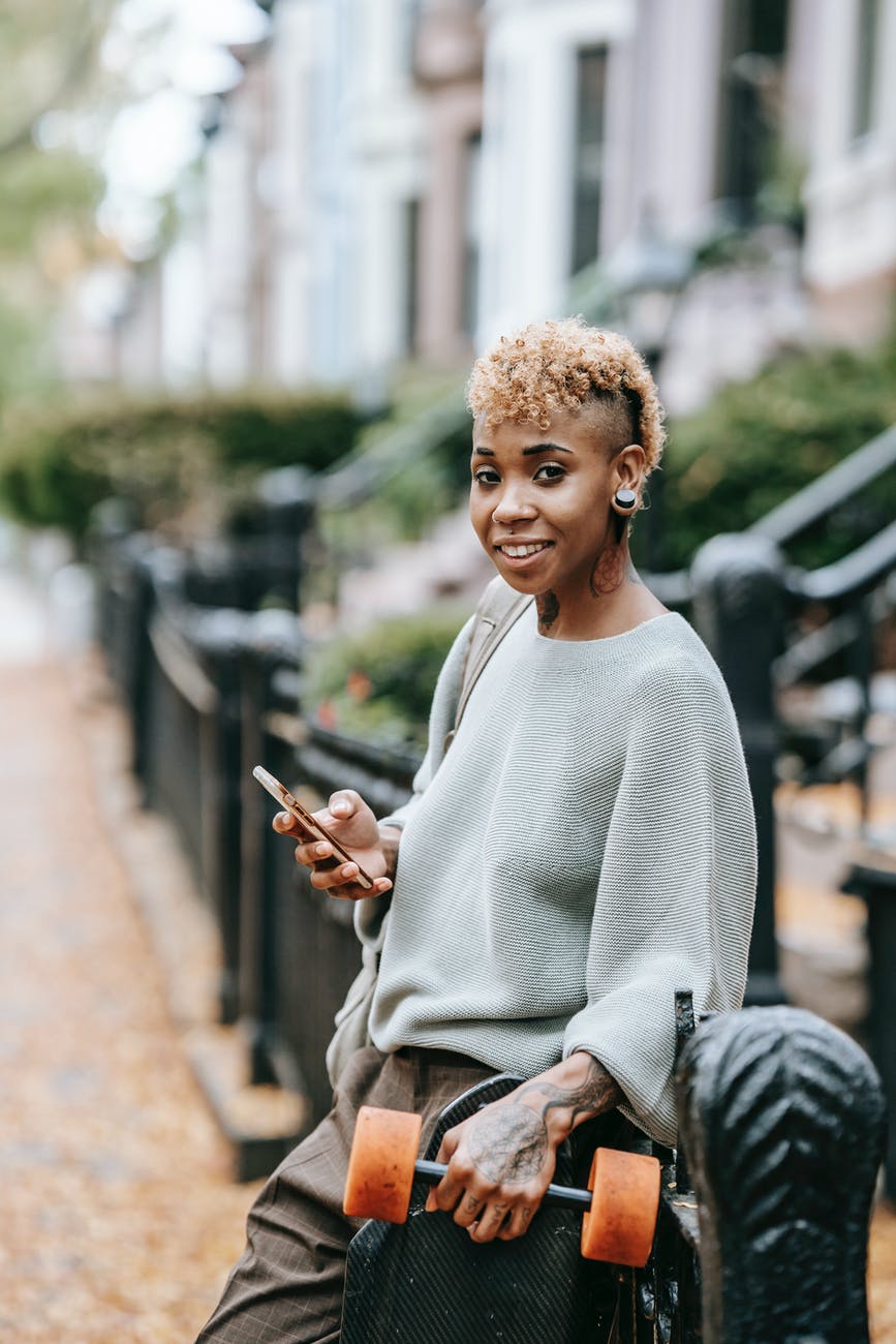 cheerful black woman with smartphone and dumbbell on street