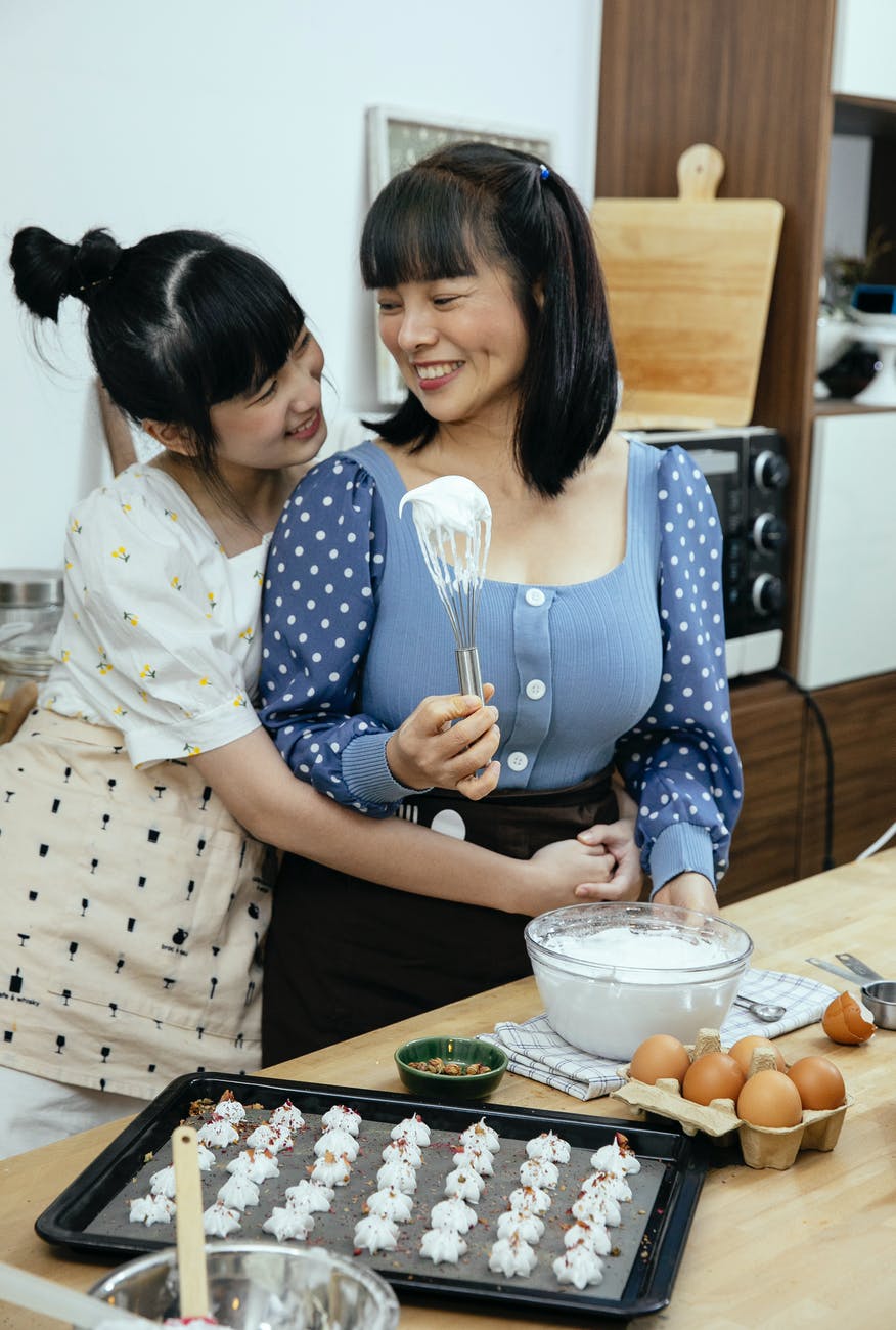 smiling asian mother with daughter preparing meringue cookies at home