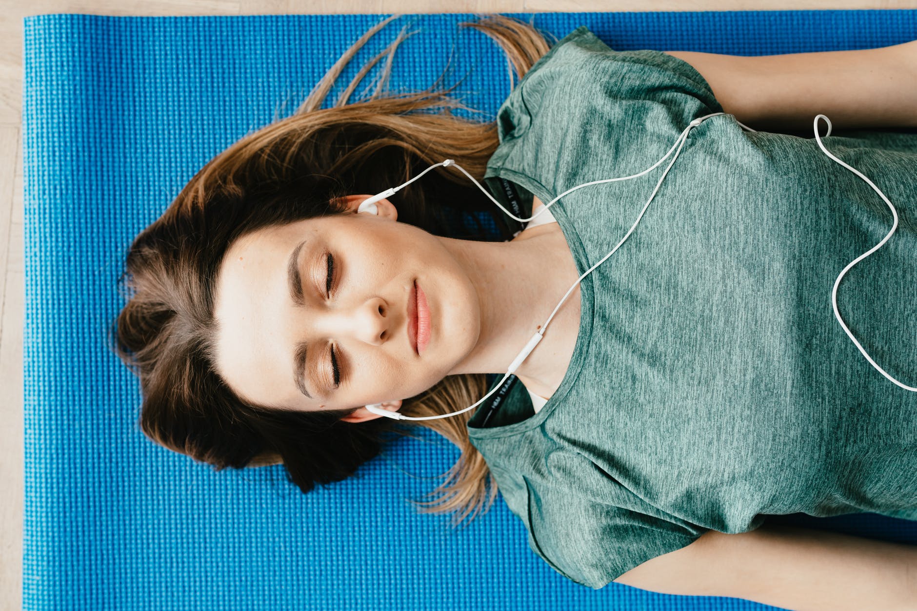 tranquil woman resting on yoga mat in earphones at home