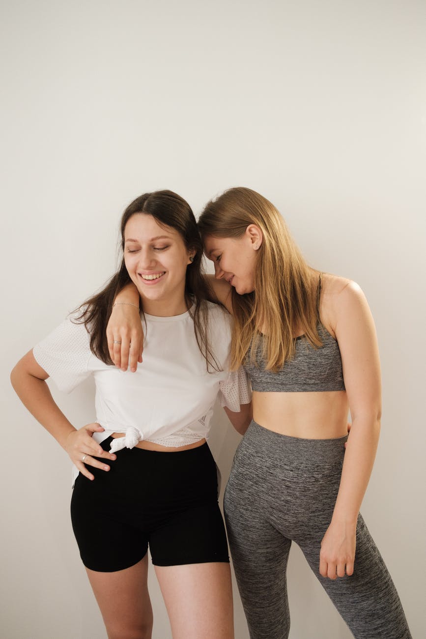 happy young girlfriends hugging against white background after workout