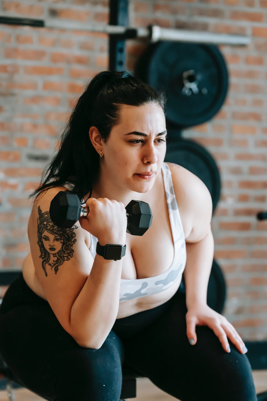 focused overweight female lifting dumbbell in training studio