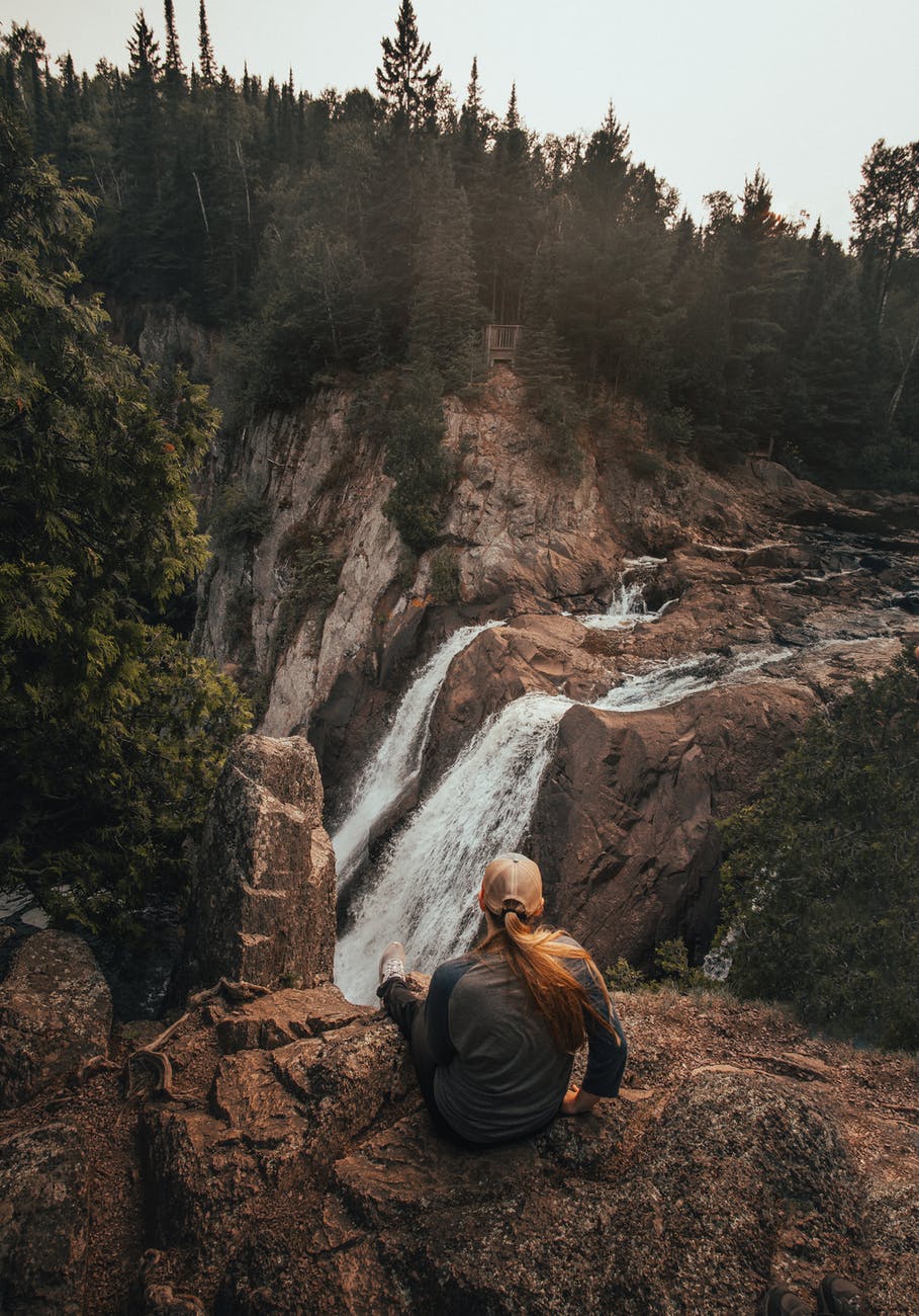 woman sitting on rock while staring on waterfall